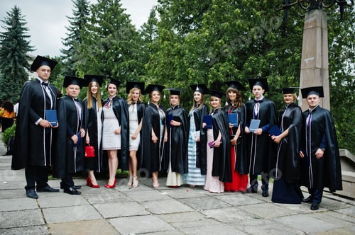 Preview: Huge group of graduates in graduation gowns and caps posing outdoor.