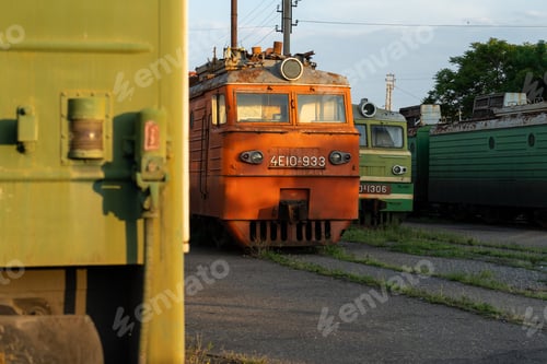 Preview: Decommissioned orange and green soviet locomotives stand on overgrown railway in abandoned stock