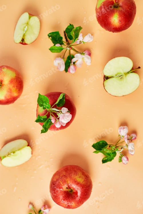Preview: Sliced, whole red apple and flowers a flat lay on a pastel orange background