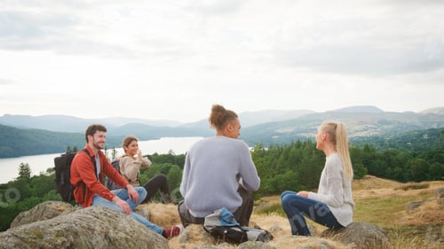 Preview: Multi-Cultural Group Of Young Friends Resting At Top Of Hill On Hike Through Lake District UK