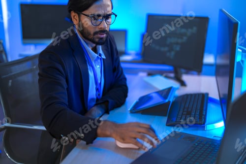 Preview: Focused Indian male AI developer coding a complex machine learning algorithm late