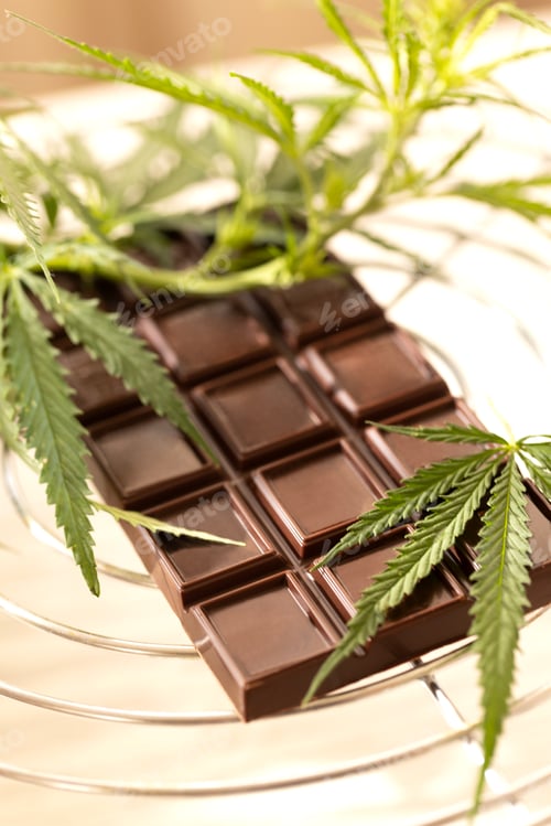 Preview: Dark chocolate bar placed beside fresh cannabis leaves on a marble background