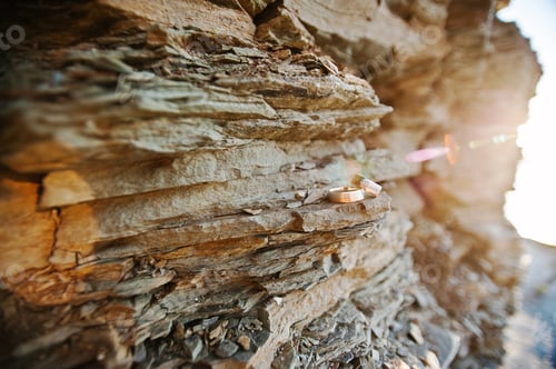 Preview: Wedding rings on stone of rock on sunset