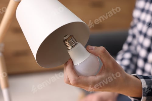 Preview: Man changing light bulb in lamp at home, closeup
