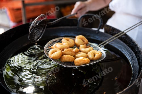 Preview: Cook holds a serving of freshly baked donuts on sieve, just lifted from the oil
