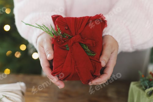 Preview: Zero waste christmas gift. Woman holding christmas present in red cloth on rustic table