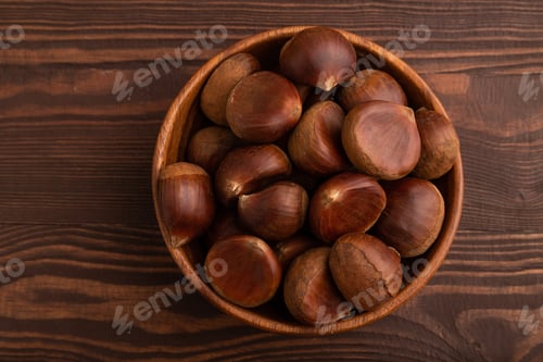 Preview: wooden bowl with raw edible Сhestnuts on brown wooden, top view, flat lay, close up, minimalism