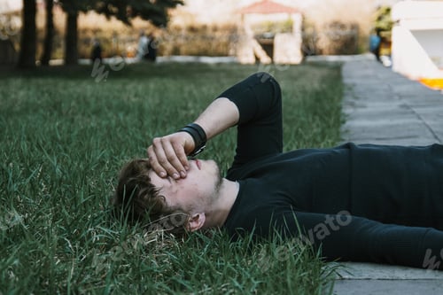 Preview: upset guy lies on the lawn and covers his face with his hand