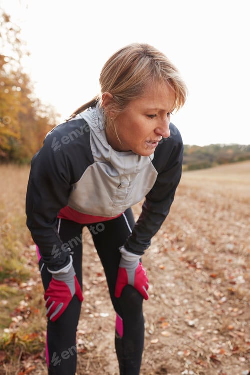 Preview: Mature Female Runner Pausing For Breath During Exercise In Woods