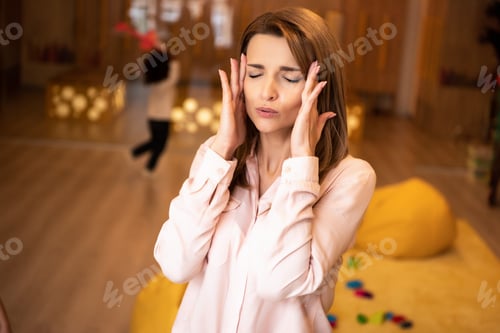 Preview: tired educator with closed eyes touching head in kindergarten, kid running in room