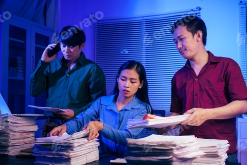 Preview: Three young businessmen work together in office at night, busy on their laptops,checking documents