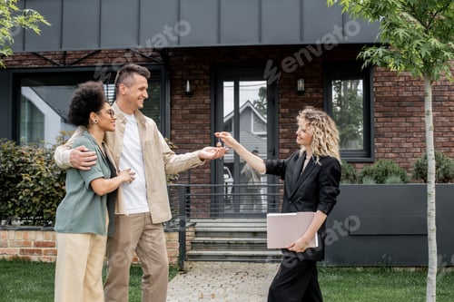 Preview: real estate broker with folder giving key to overjoyed interracial couple near new city cottage
