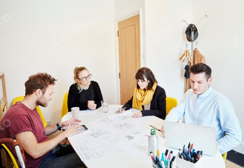 Preview: Four people at a business meeting around a table spread with papers, one man using a tablet and one