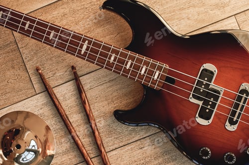Preview: Top view of electronic guitar with wooden sticks and golden cymbal lying on wooden background