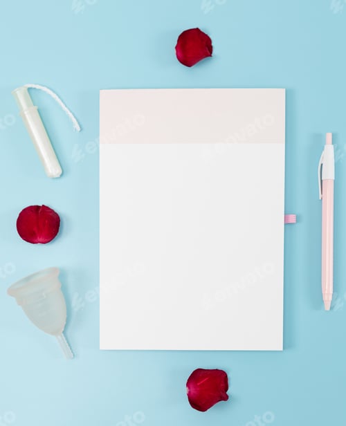 Preview: Empty notebook, menstrual cup, tampon and rose petal on a blue background.