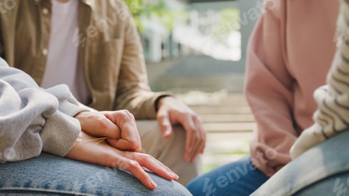 Preview: Close-up men and women group sit in circle hold hands together hope for help people in park.