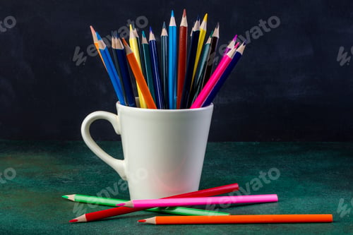 Preview: side view of a bunch of colored pencils in a white cup on dark background