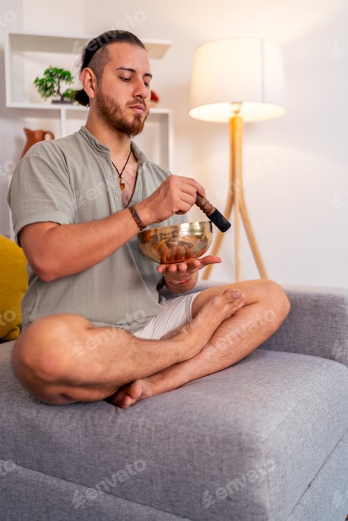 Preview: Young man practicing yoga and meditation with tibetan singing bowl at home