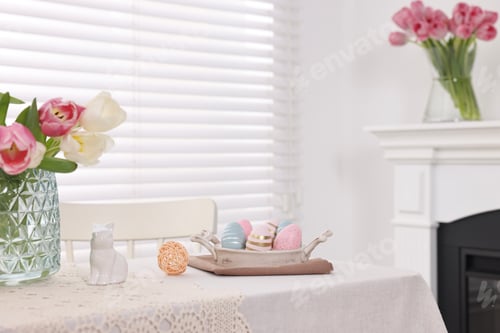 Preview: Easter decorations. Bouquet of tulips in vase, painted eggs and bunny figure on white table at home