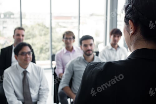 Preview: Asian woman offering information to people on the team in meeting.