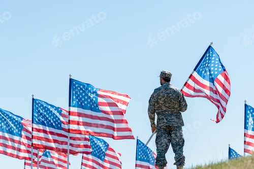 Preview: selective focus of man in military uniform and cap standing and holding american flag