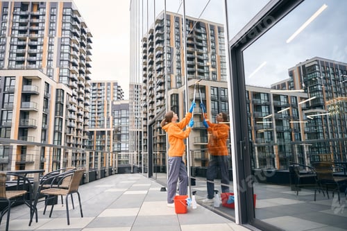 Preview: Pretty cleaning company employee in a warm sweatshirt washes mirrored windows