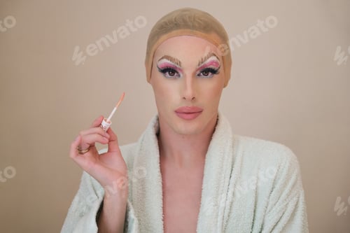 Preview: Drag queen person with lip gloss brush wearing bathrobe and looking at camera.
