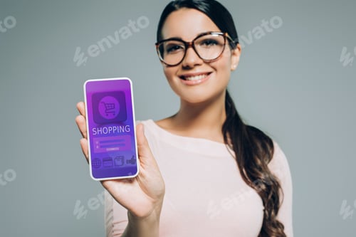 Preview: beautiful woman presenting smartphone with online shopping appliance, isolated on grey