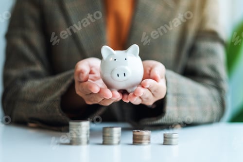 Preview: a businesswoman holding piggy bank with stack of coins on the table for saving money