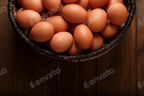 Preview: Raw chicken eggs in wicker basket on wooden table, top view. Space for text