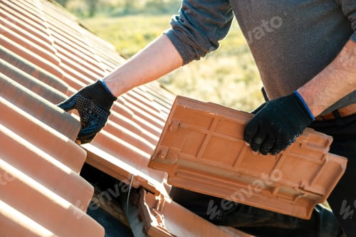 Preview: Closeup of worker hands installing yellow ceramic roofing tiles mounted on wooden boards