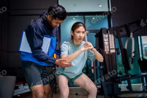 Preview: Woman Squatting with Trainer in Gym