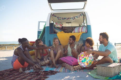 Preview: Front view of group of diverse friends interacting with each other near camper van at beach