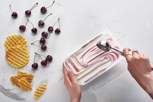 Preview: cropped view of woman with delicious ice cream and spoon near waffles and cherries on marble grey
