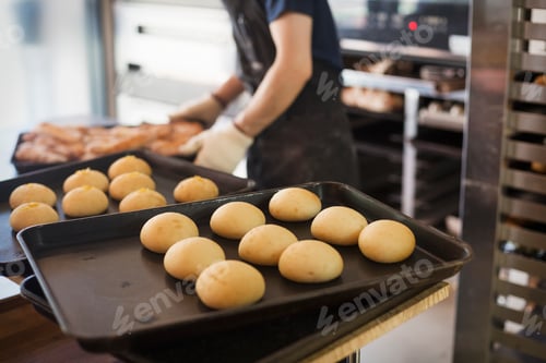 Preview: Person working in a bakery, placing freshly baked rolls on large trays.