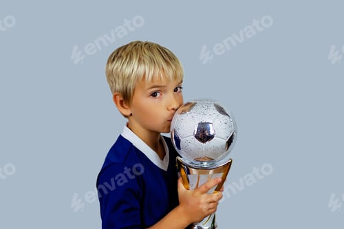 Preview: Young soccer player in blue jersey holds winners cup after the goal, isolated at light background