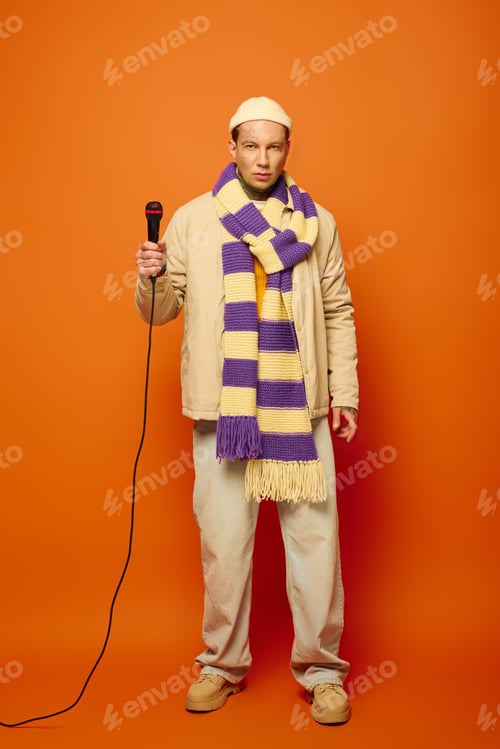 Preview: Young man with tattoos confidently holding a microphone against a vibrant orange backdrop