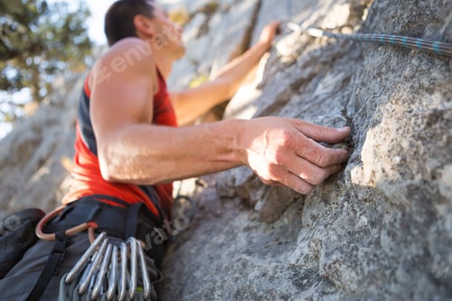 Preview: Climber in red t-shirt climbs a gray rock. A strong hand grabbed the lead