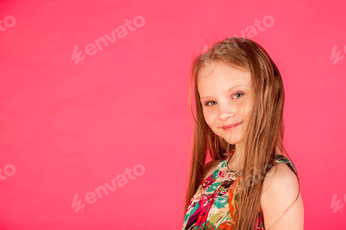 Preview: Face of smiling little girl in colorful t-shirt posing at pink background