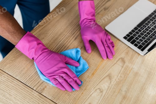 Preview: Cropped view of african american cleaner in rubber gloves cleaning table near laptop in office