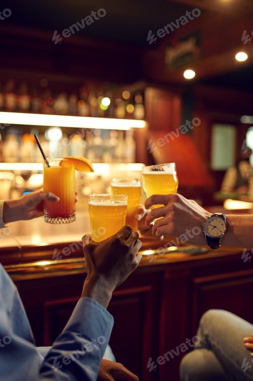 Preview: Friends clink glasses with beer at counter in bar