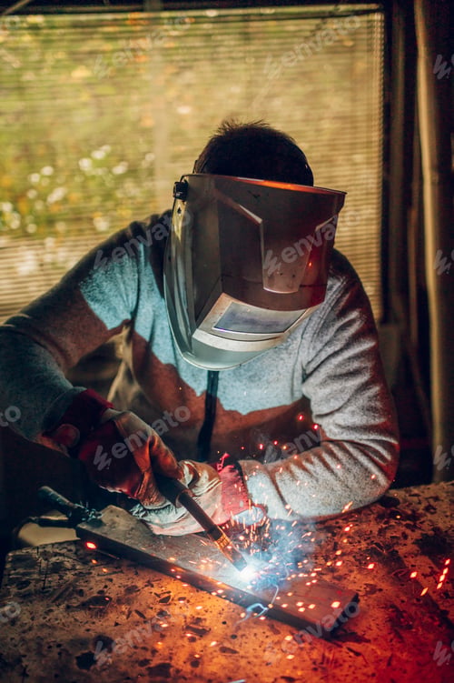 Preview: Man worker welding metal with welding machine in a factory or workshop