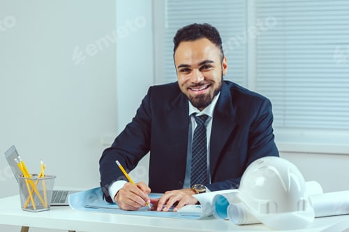 Preview: Man working on construction plans in an office setting with tools and computer nearby