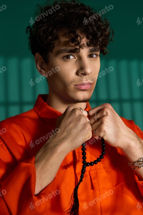 Preview: Curly-haired man in trendy outfit poses confidently in stylish studio setting