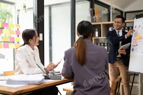 Preview: Business adviser explaining business plan strategy on flipchart to colleagues, male coach or