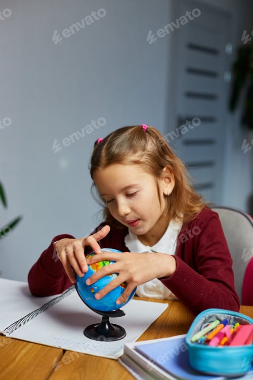 Preview: Happy schoolgirl at workplace studying globe in classroom