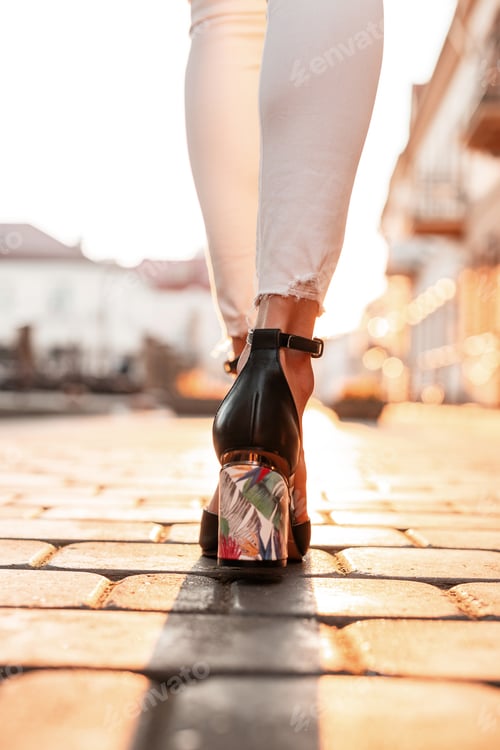 Preview: Female legs in white jeans in elegant leather sandals walks in the city at sunset. Top view