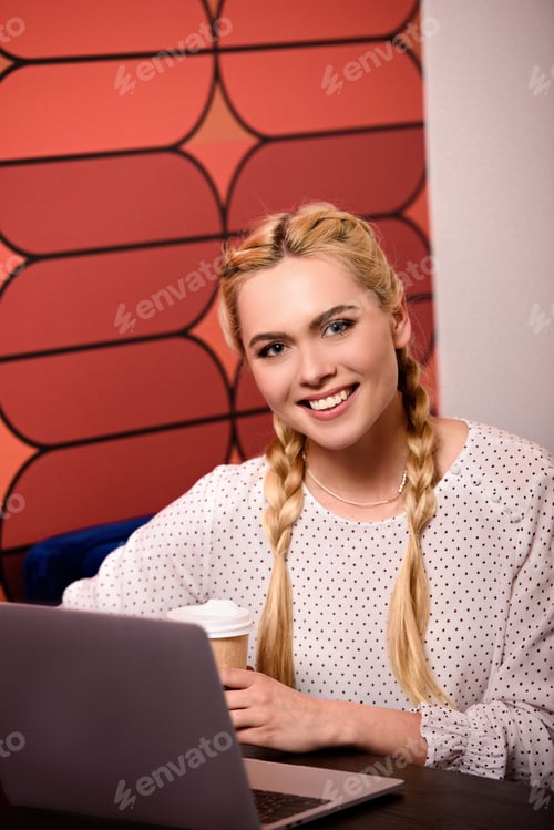 Preview: smiling young businesswoman sitting at table with laptop and coffee cup in modern office