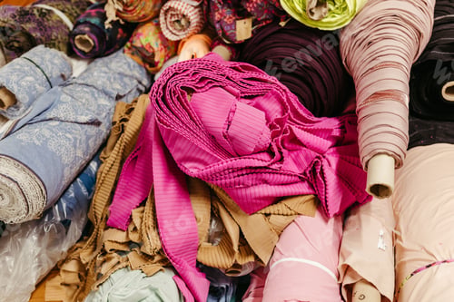 Preview: Vibrant collection of multicolored fabric rolls and swatches, arranged in a neat pile