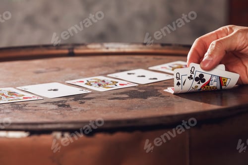 Preview: Close-up of mans hand showing his cards with two ladies card while playing poker on barrel